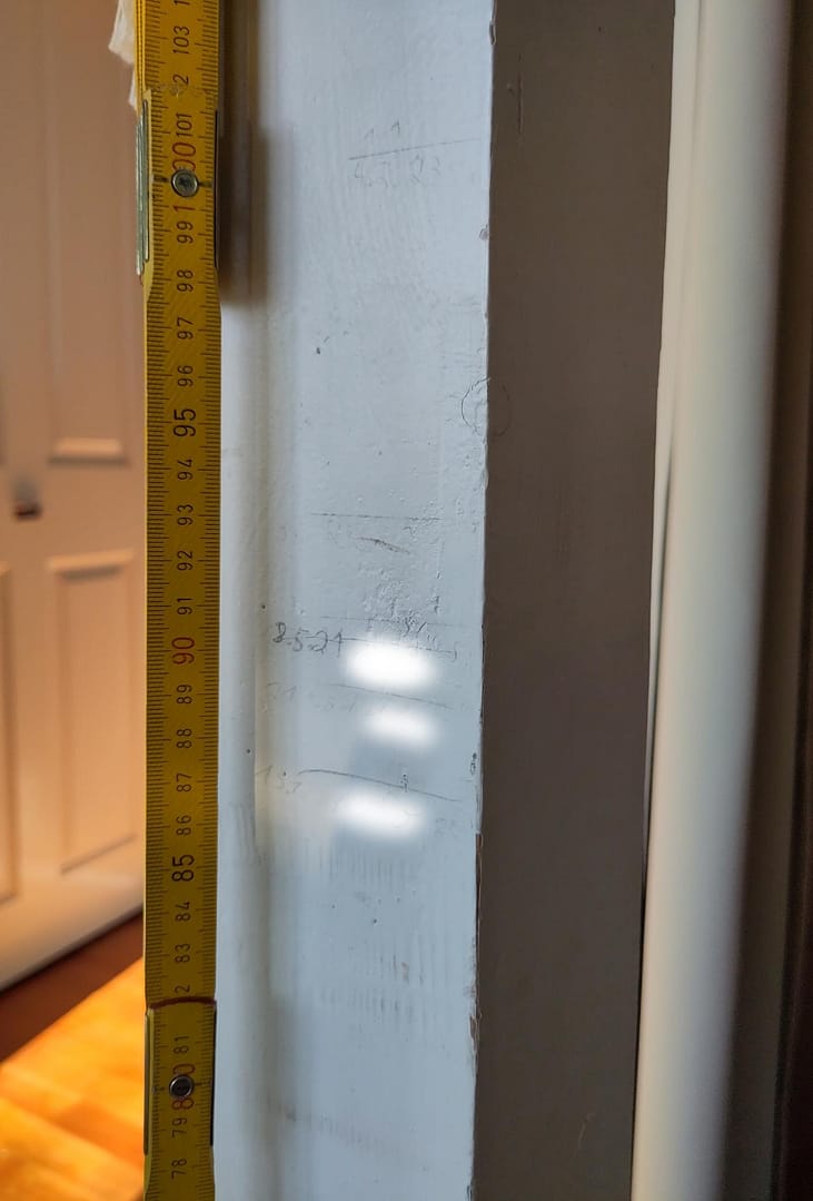 ein weißer Balken mit Messmarkierungen, daran gelehnt ein Zollstock